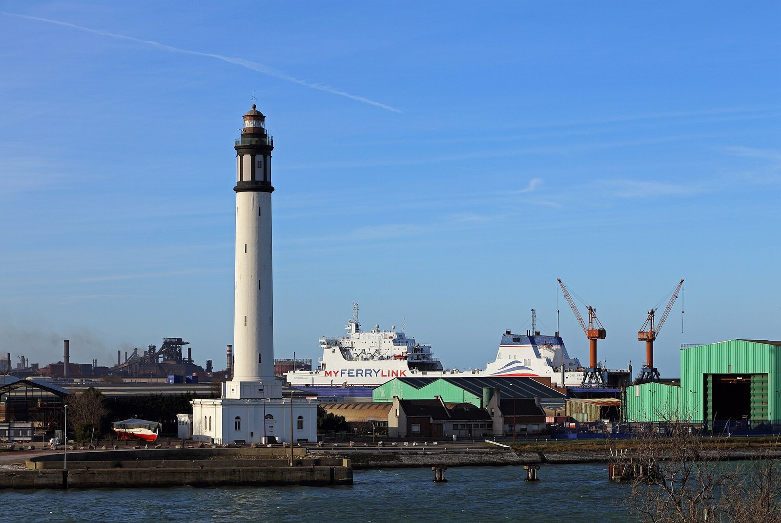 Le phare du Risban veille sur le port de Dunkerque, un ferry transmanche à quai et les grues du chantier alignées sous un ciel d’hiver.